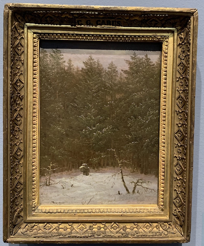 An old stone cross on a clearing in front of a row of sprout trees, dusky light, snow covers the scene.