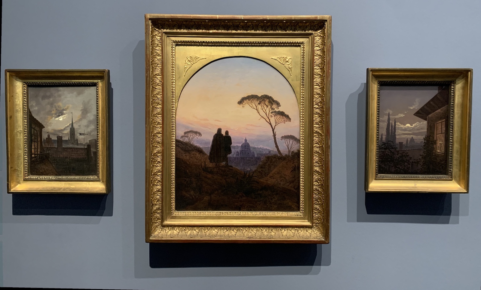 Three paintings by Carl Gustav Carus. Left and right a moonlit night, partially cloudy sky, over a city in the distance; centre: two men watching Rome in the dusk from a distance.
